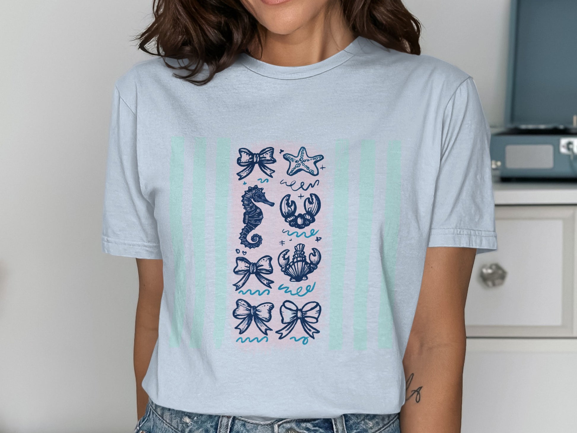 Light blue t-shirt with navy blue bows, starfish, seahorse, and crab illustrations.