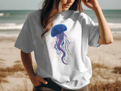 White t-shirt with a purple and blue jellyfish graphic, on a beach background.