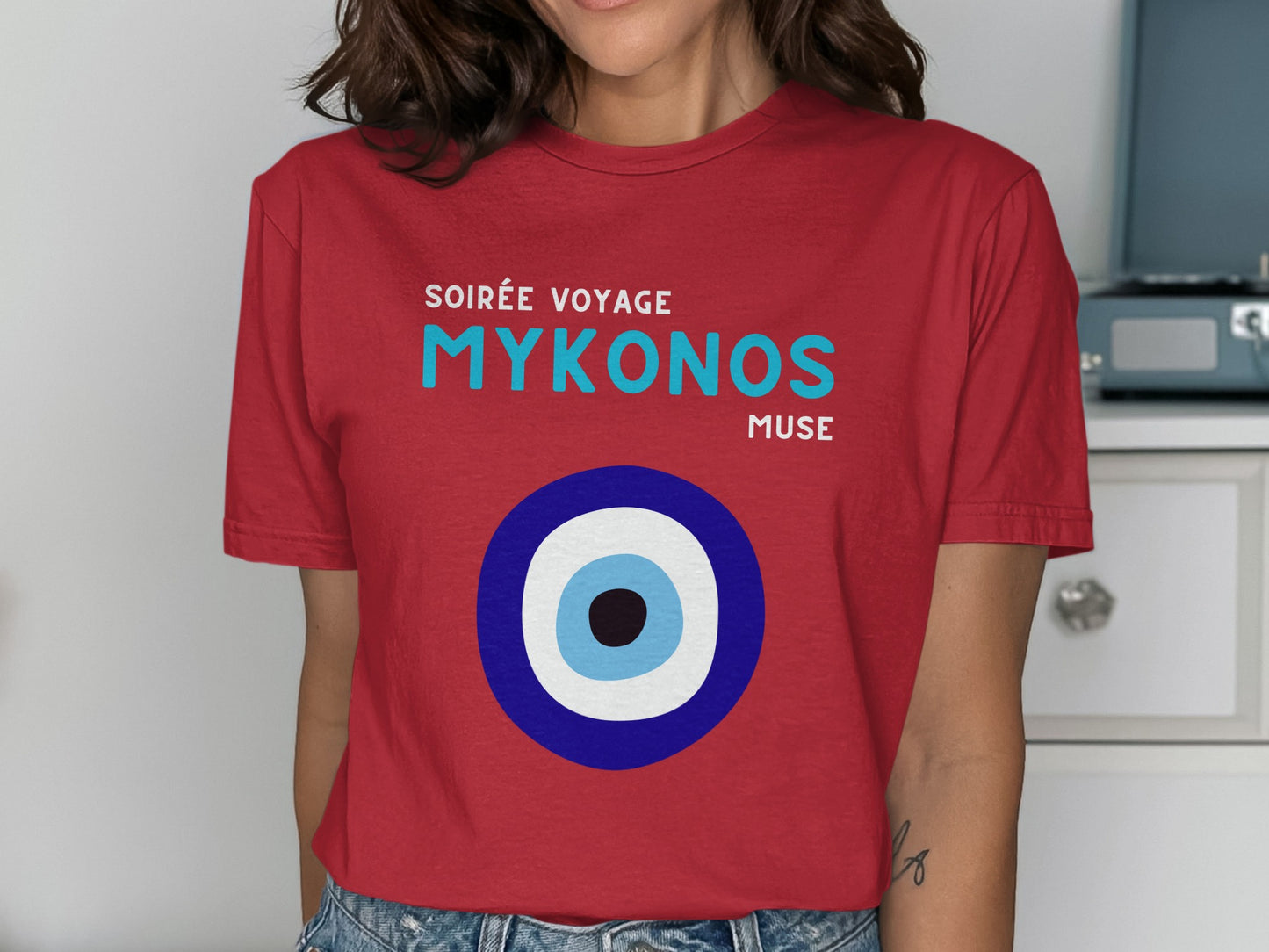 Red t-shirt with "SOIRÉE VOYAGE MYKONOS MUSE" and an evil eye graphic.
