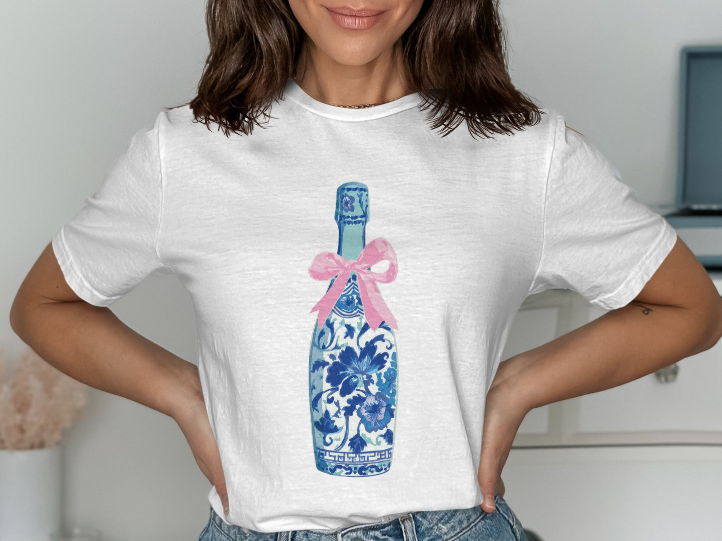 White t-shirt with blue and white floral champagne bottle graphic and pink bow.