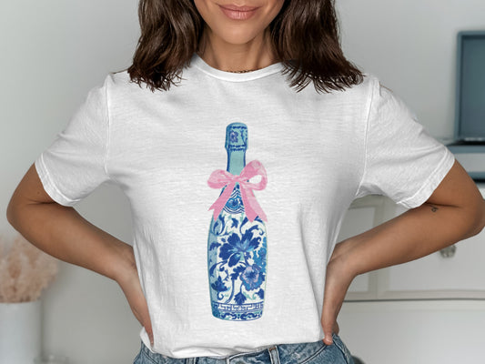 White t-shirt with blue and white floral champagne bottle graphic and pink bow.