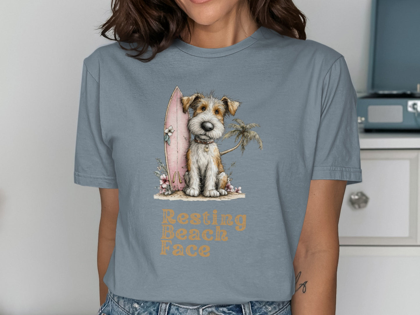 Scruffy terrier dog with surfboard and palm tree graphic on t-shirt.