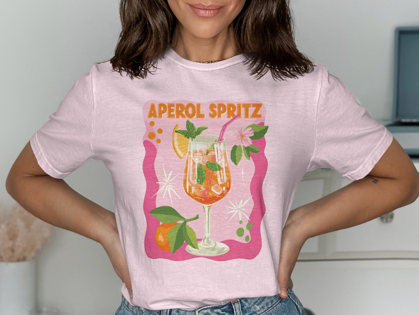 Pink t-shirt with "Aperol Spritz" graphic of a cocktail with orange slice and mint.