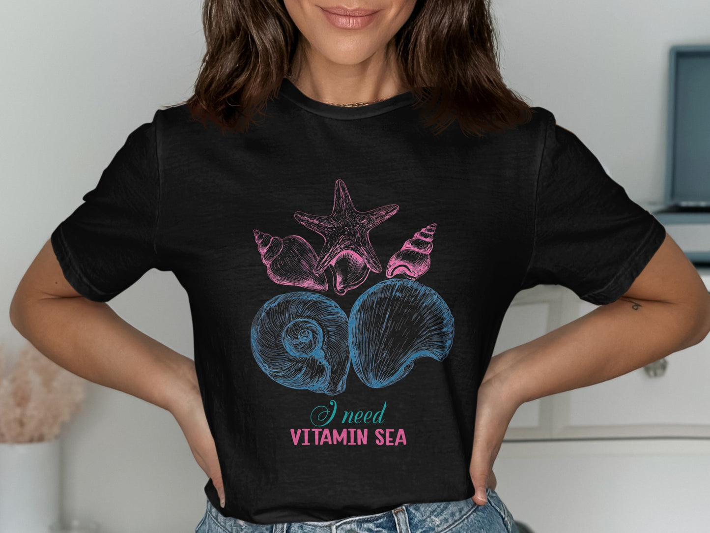 Black t-shirt with pink and blue seashells and starfish graphic and text.