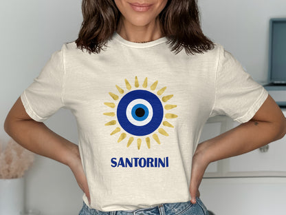 Cream t-shirt with a blue and gold evil eye design and "SANTORINI" text.