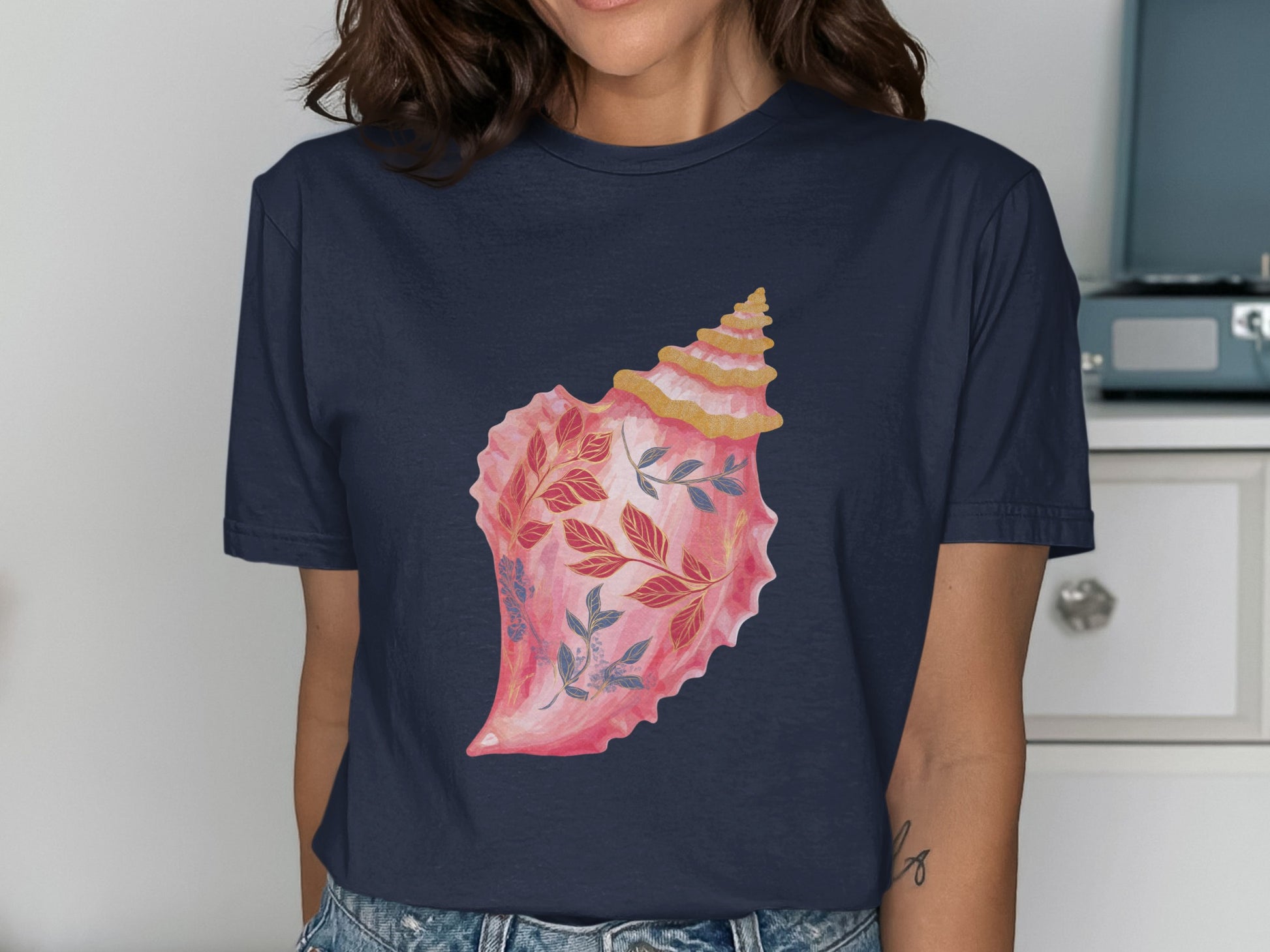 Navy t-shirt with a watercolor illustration of a pink conch shell with blue and red leaves.