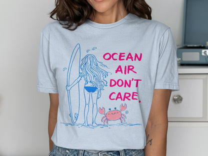 T-shirt with a drawing of a surfer girl and a crab, text reads "OCEAN AIR DON'T CARE".