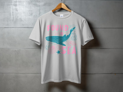 White t-shirt with pink and teal text and ocean-themed graphic.