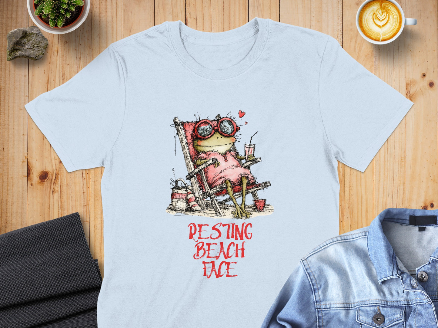 Light blue t-shirt with cartoon frog in sunglasses relaxing on a beach chair.