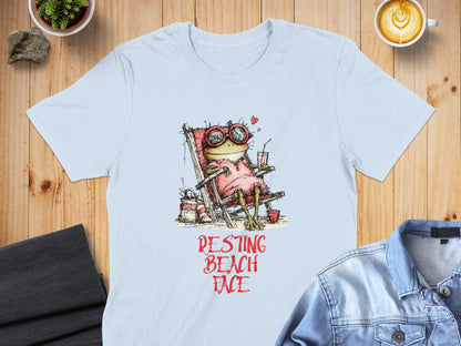 Light blue t-shirt with cartoon frog in sunglasses relaxing on a beach chair.