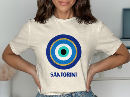 Cream t-shirt with a blue, gold, and white evil eye design and "SANTORINI" text.
