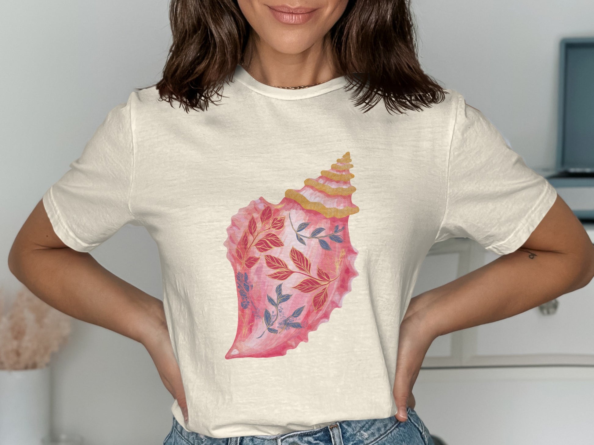 Cream t-shirt with a pink seashell graphic featuring blue and red floral accents.