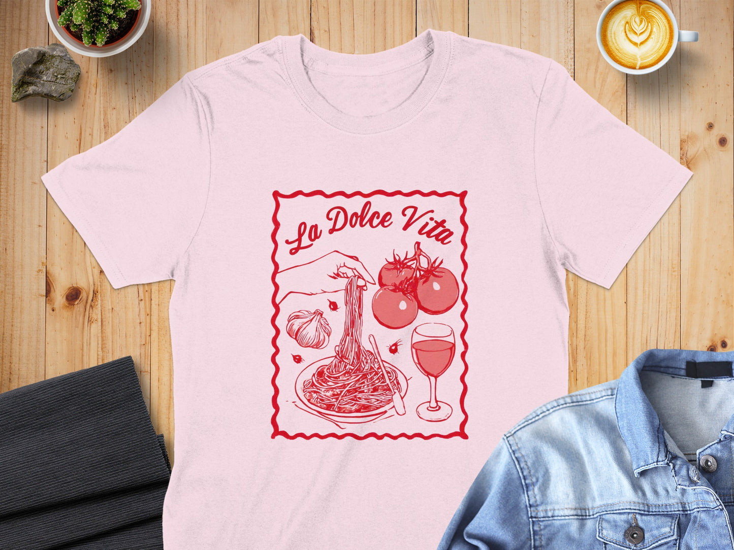 Pink t-shirt with "La Dolce Vita" text and pasta, tomatoes, garlic, and wine illustration.