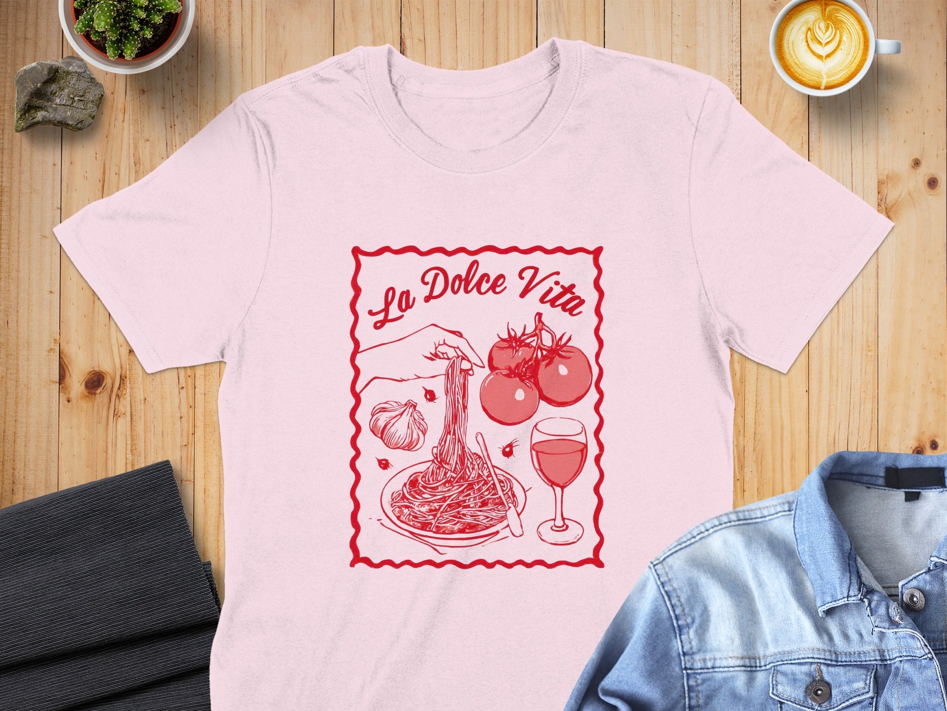 Pink t-shirt with "La Dolce Vita" text and pasta, tomatoes, garlic, and wine illustration.