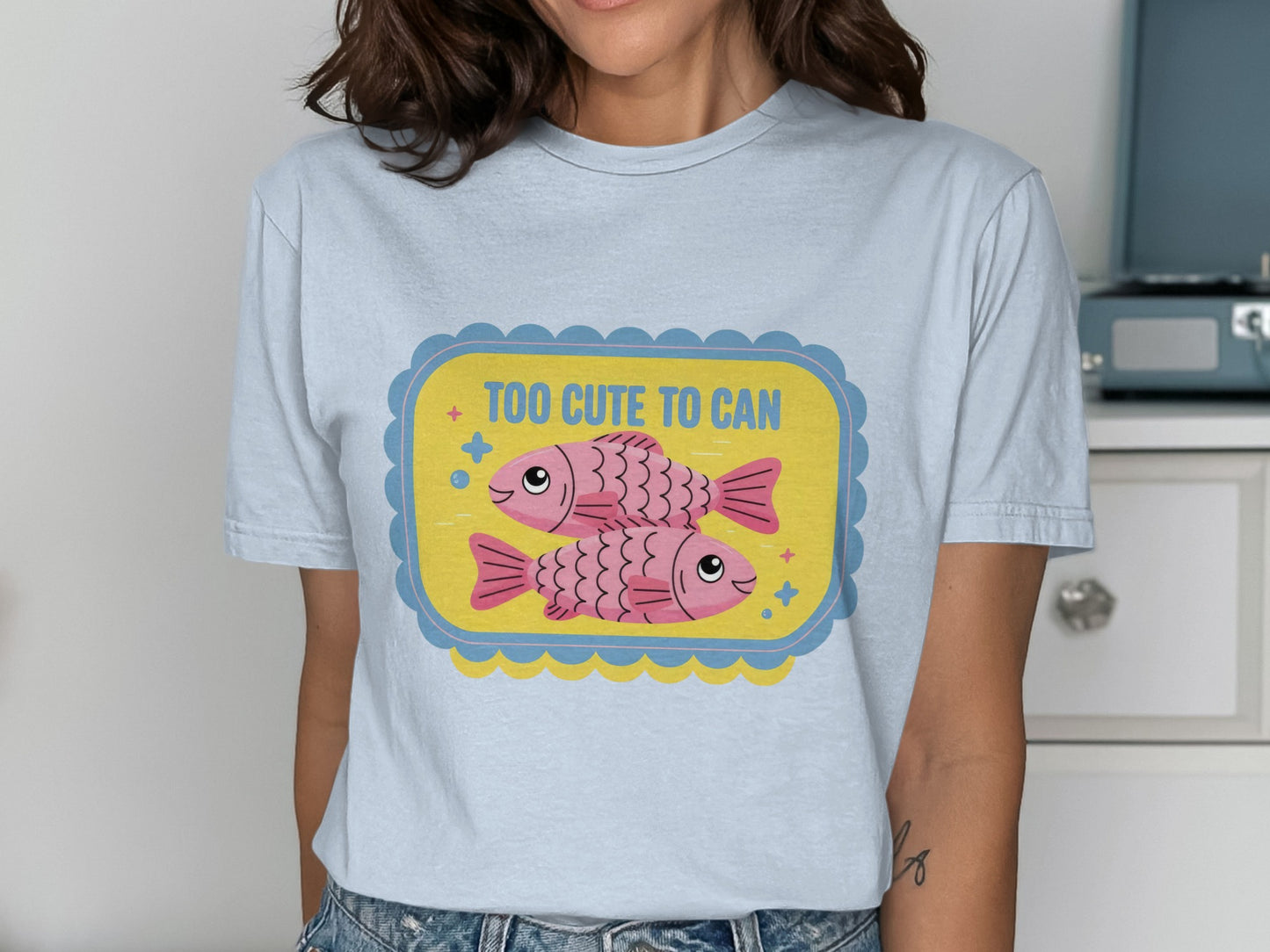 Light blue t-shirt with pink fish graphic and text "TOO CUTE TO CAN".