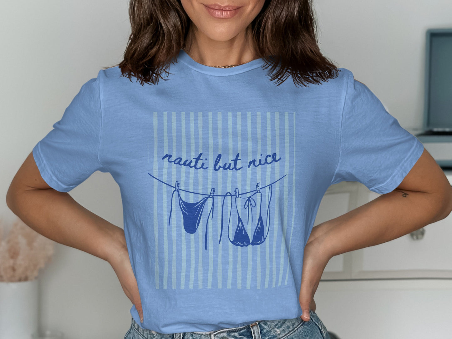 Light blue t-shirt with "nauti but nice" text and bathing suits drying on a clothesline.