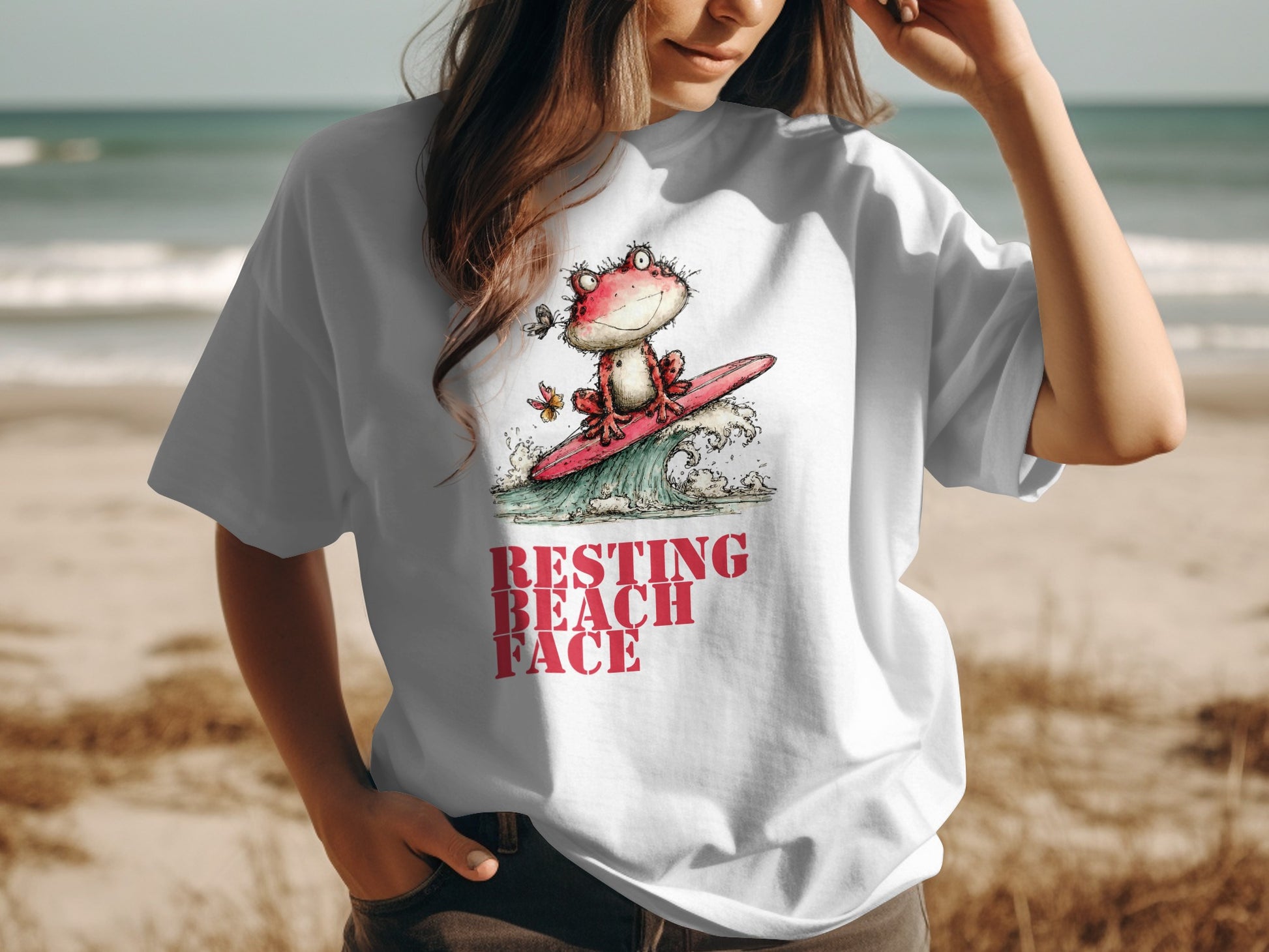 White t-shirt with cartoon frog surfing and text "RESTING BEACH FACE".