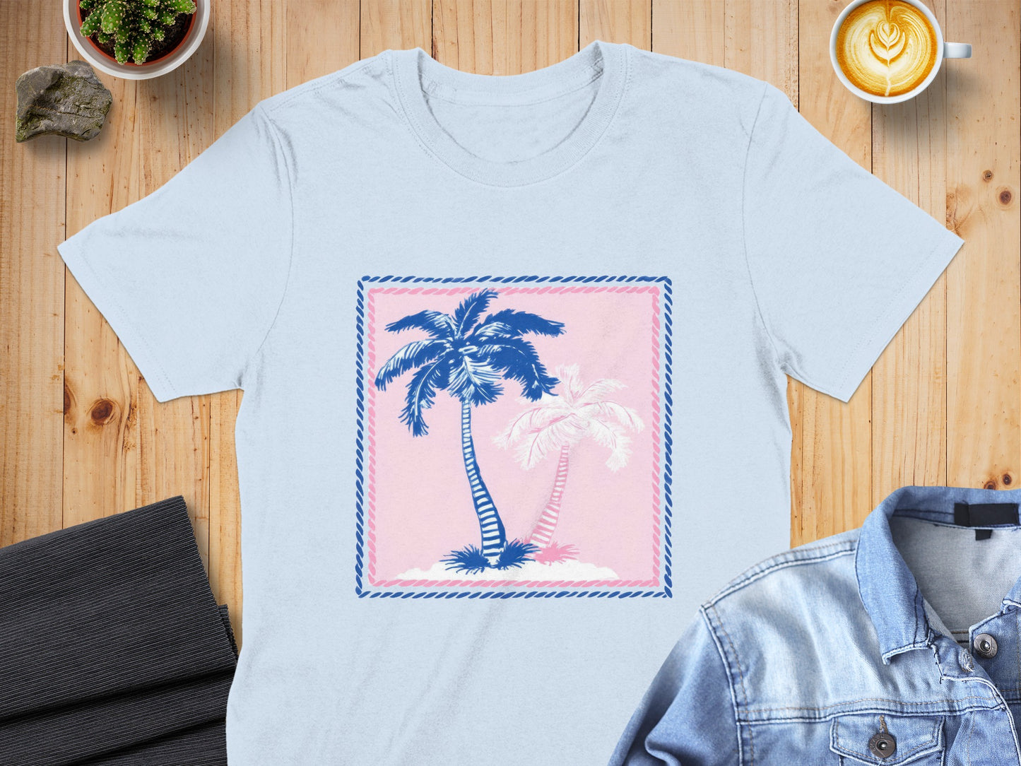 Light blue t-shirt with pink and blue palm trees graphic in a pink and blue border.