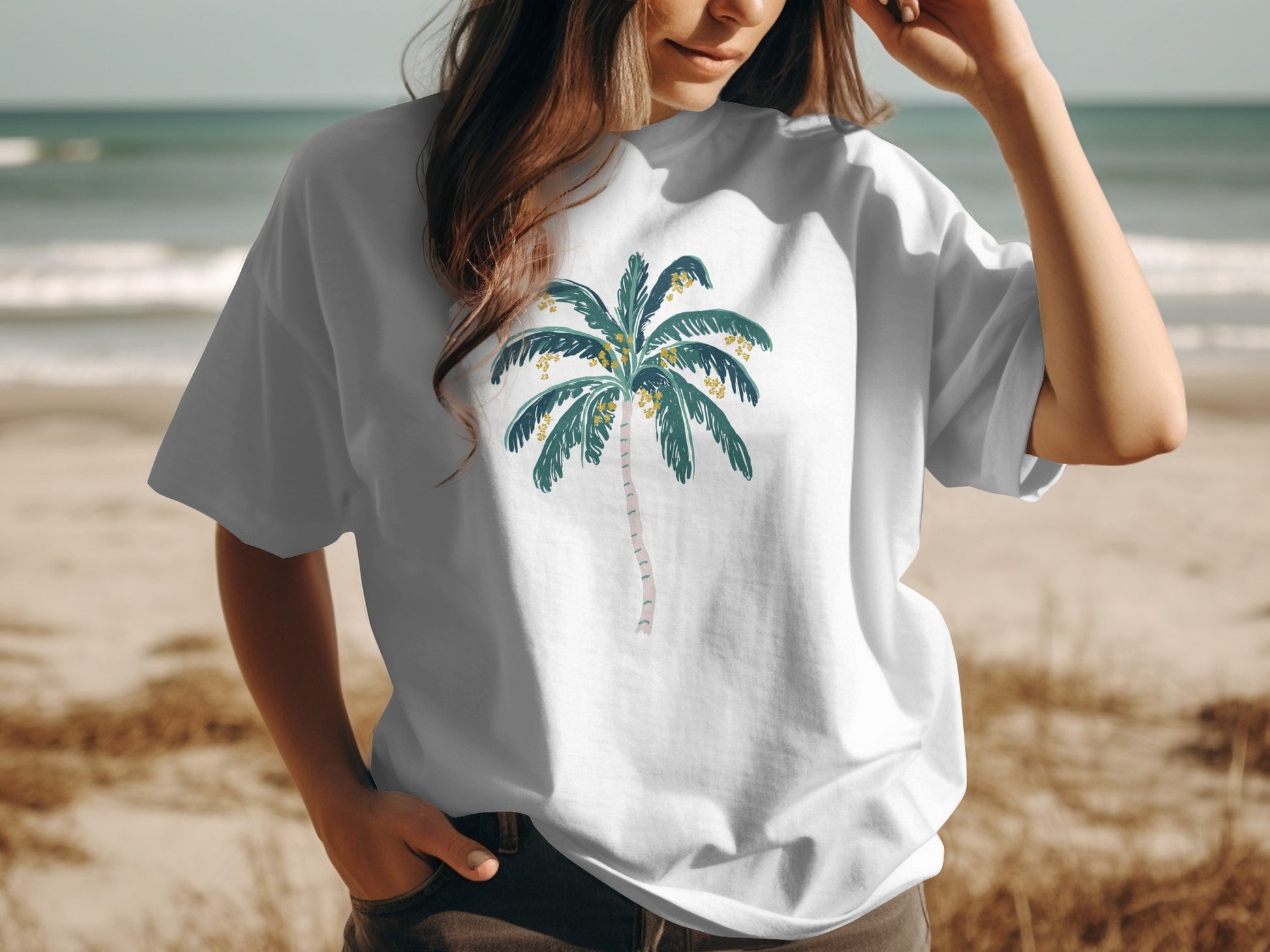 White t-shirt with a cartoon palm tree graphic, worn by a person at the beach.