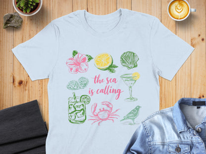 T-shirt with pink and green illustrations of beach items and text "the sea is calling".