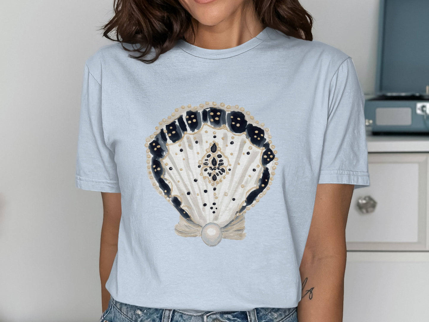 Light blue t-shirt featuring a decorative seashell with a pearl.