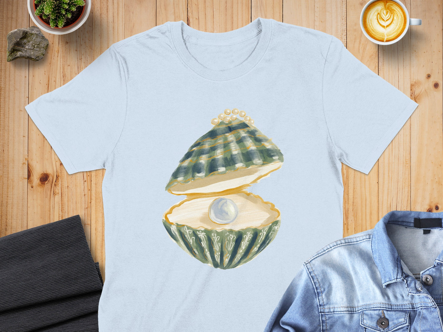 Light blue t-shirt with an open oyster holding a pearl and green shell detail.