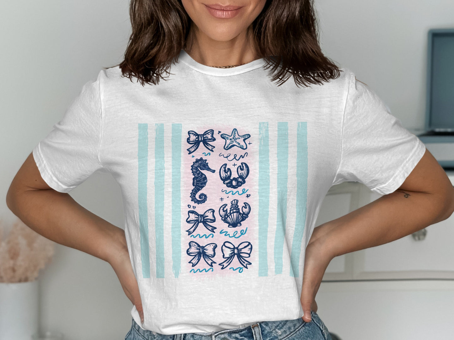 White t-shirt with blue and pink stripes featuring nautical icons: bows, seahorse, lobster, and starfish.