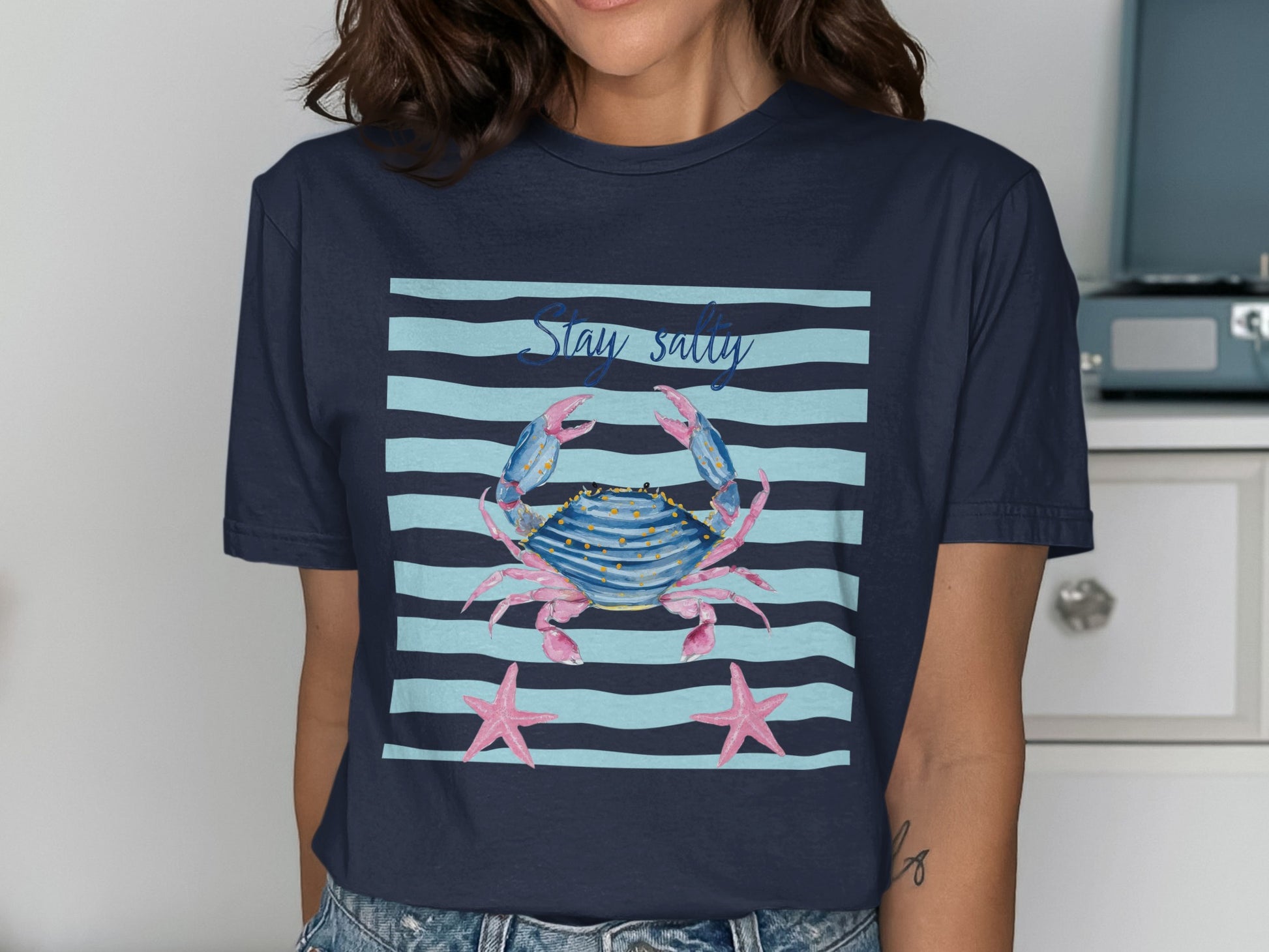 Navy t-shirt with a watercolor crab and starfish graphic on striped background.
