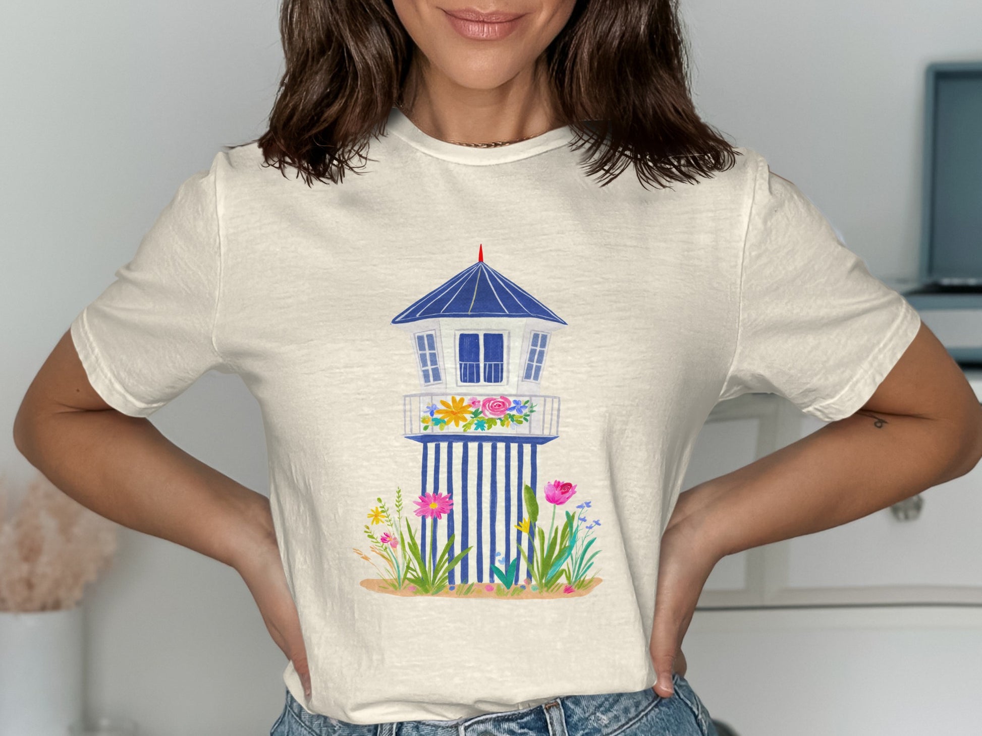 Cream t-shirt with a graphic of a blue and white beach house with flowers.