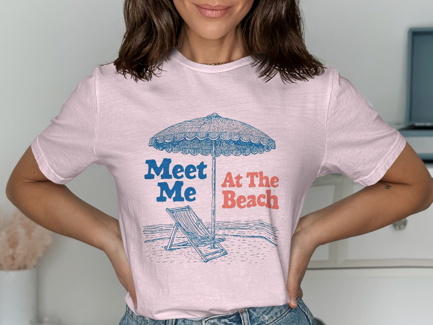 Pink t-shirt with illustration of beach chair and umbrella, text "Meet Me At The Beach".