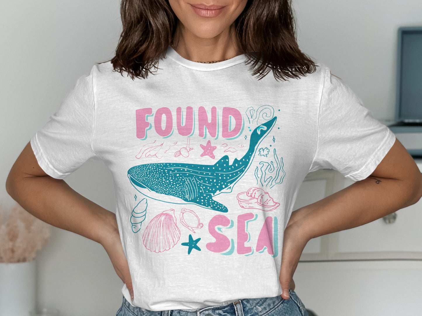 White t-shirt with a whale shark, seashells, and "FOUND IN THE SEA" text.