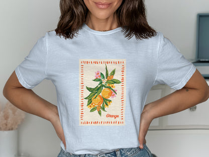 White t-shirt with orange branch and fruit design, framed by dashed lines and small flowers.
