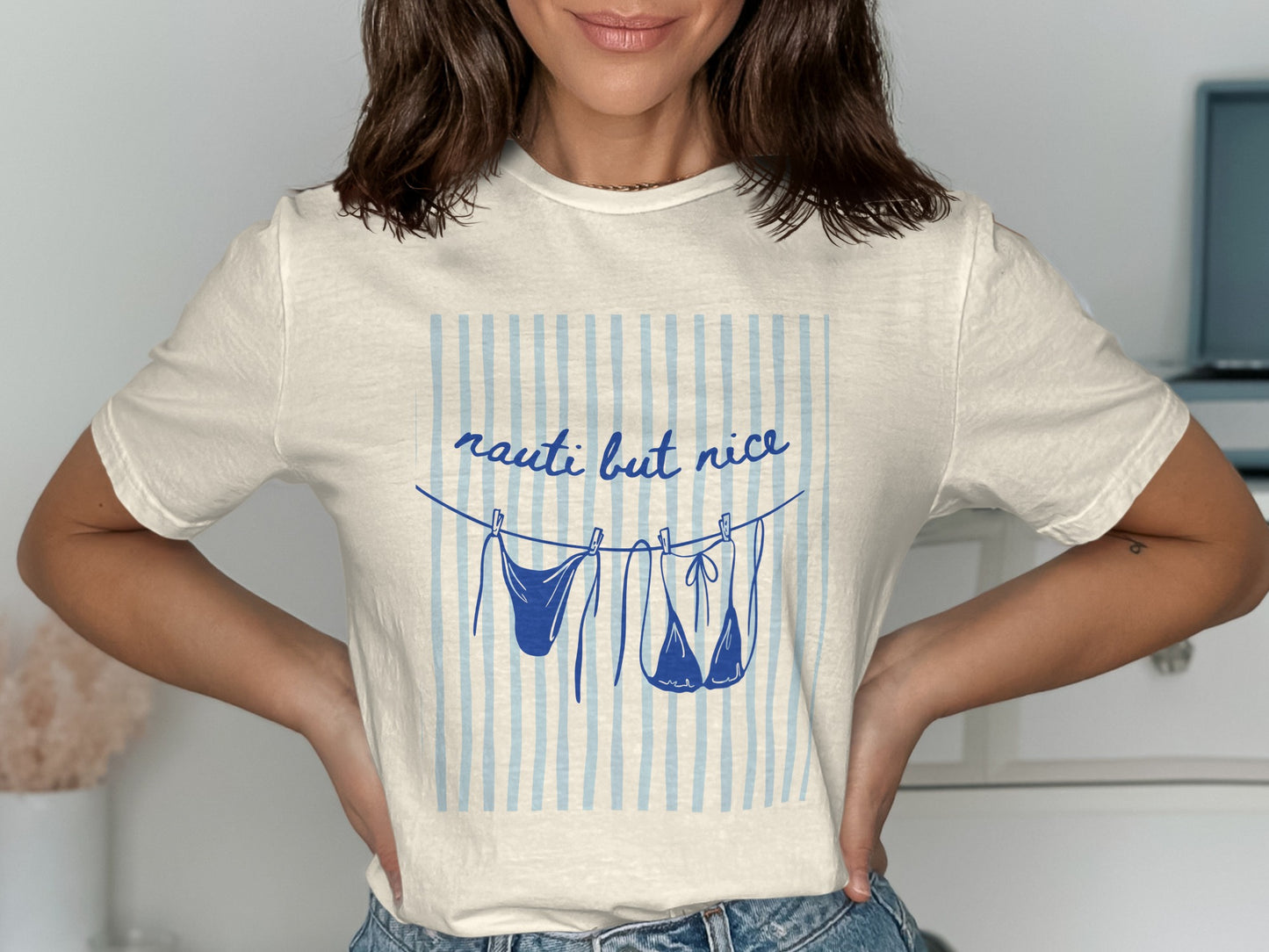 Cream t-shirt with "nauti but nice" text and bikini hanging on clothesline.