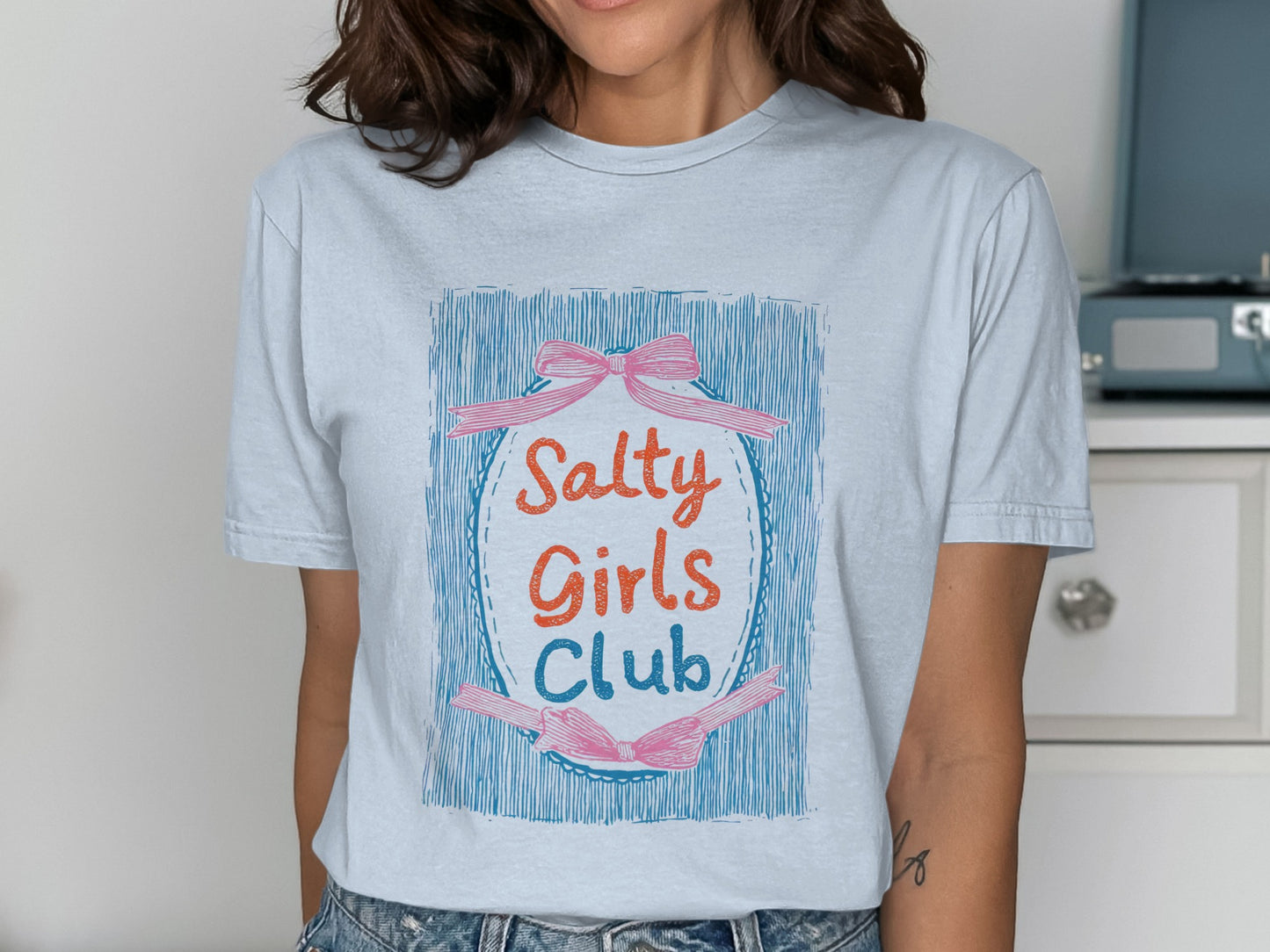 Light blue t-shirt with "Salty Girls Club" text in a colorful oval design.