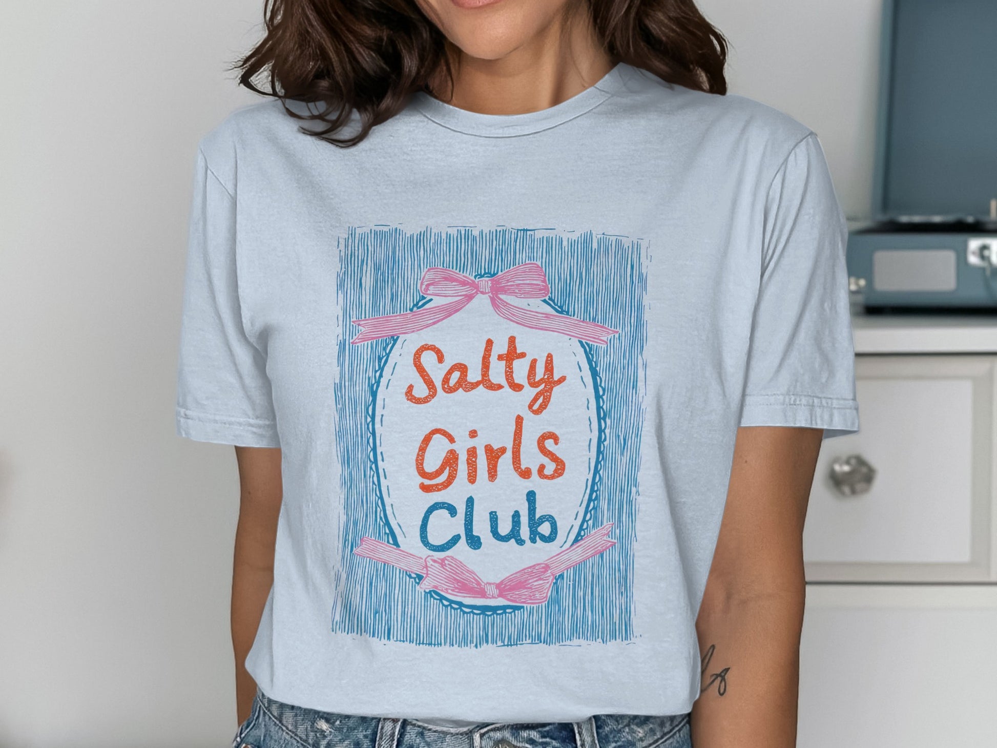 Light blue t-shirt with "Salty Girls Club" text in a colorful oval design.