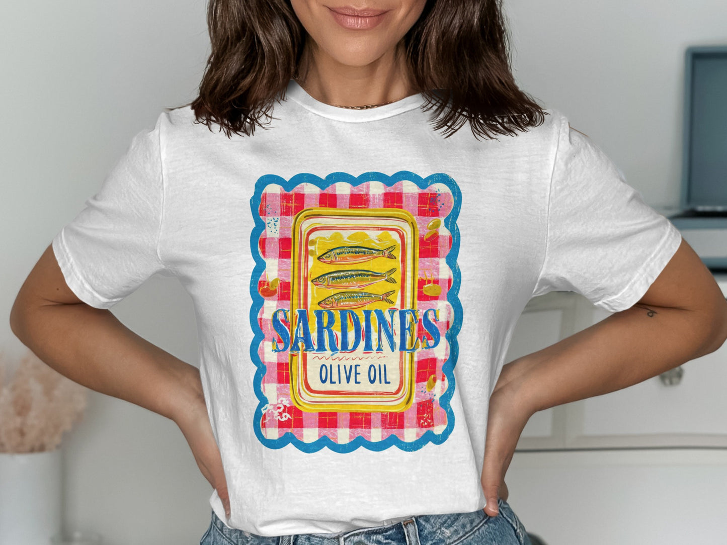 White t-shirt with a vintage sardine can label design featuring blue, yellow, and red plaid border.