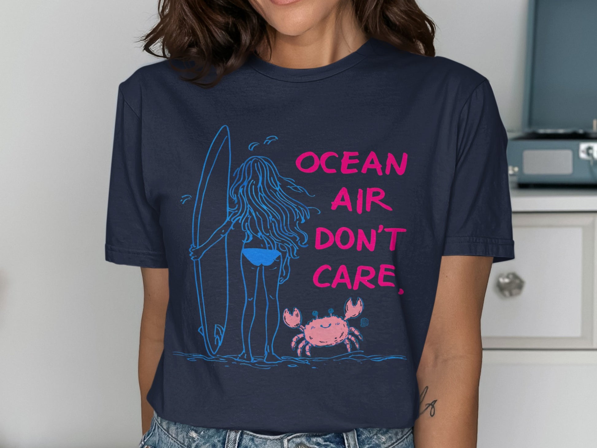 T-shirt design with a surfer girl and a crab, text "OCEAN AIR DON'T CARE".