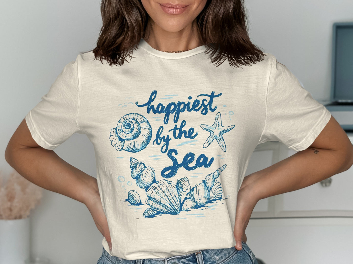 T-shirt with "Happiest by the Sea" text and blue seashell illustrations.