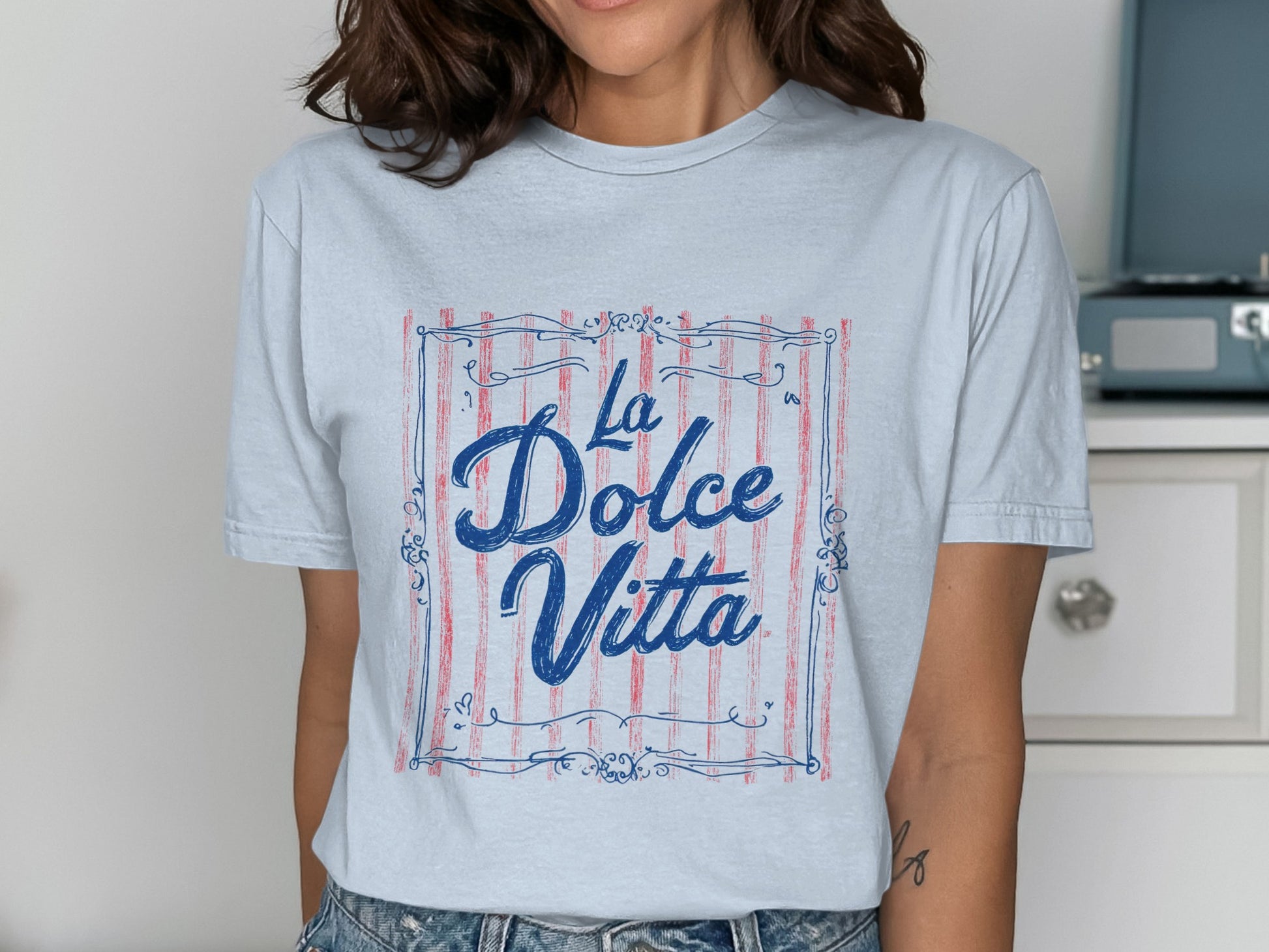 Light blue t-shirt with "La Dolce Vita" text in decorative frame.