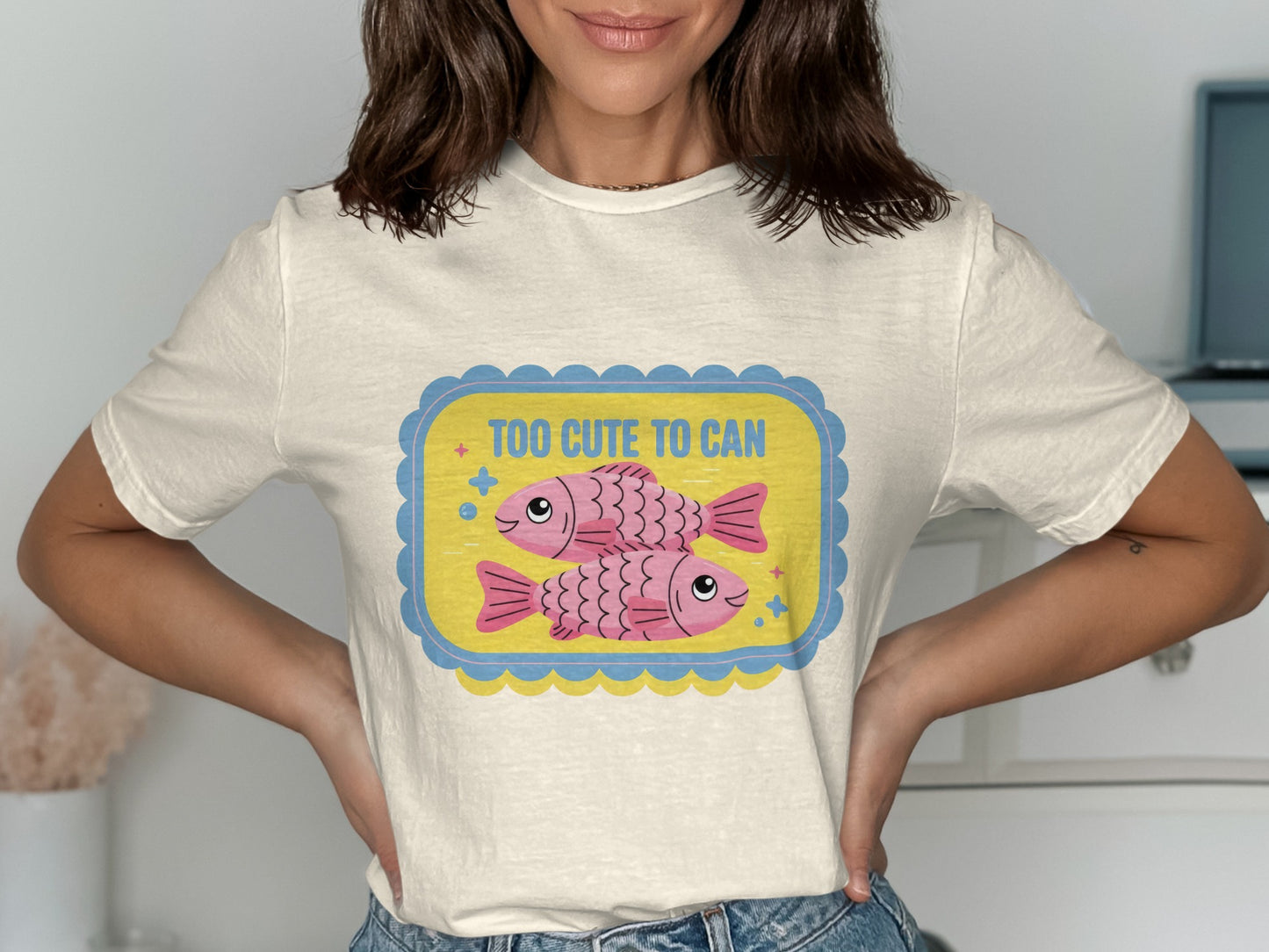 Cream t-shirt with a yellow and blue framed graphic featuring two pink fish and text.