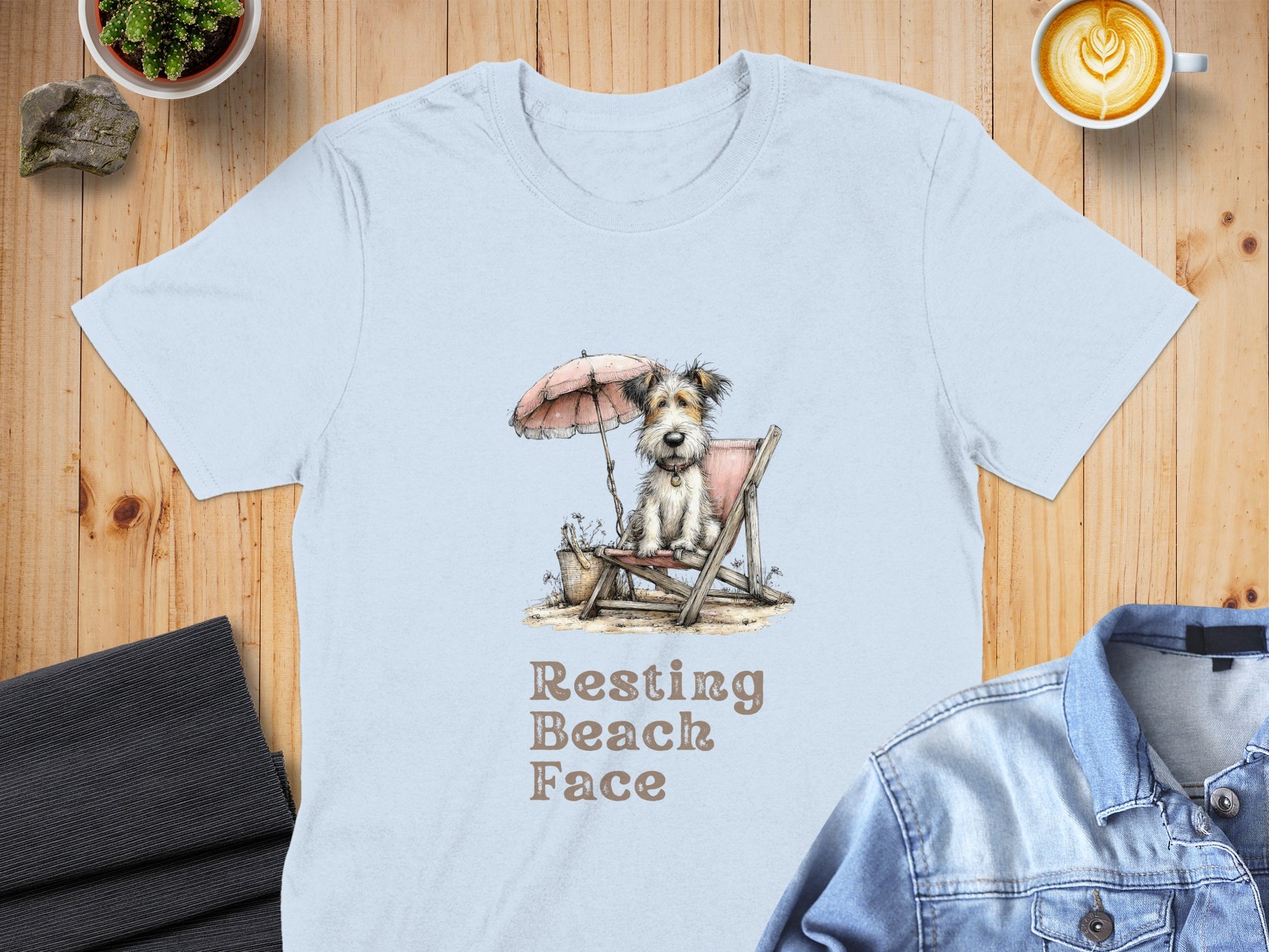 Light blue t-shirt with a cartoon dog on a beach chair under an umbrella.