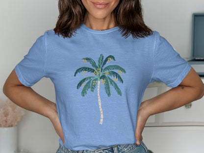 Light blue t-shirt with a stylized green palm tree and yellow fruit design.