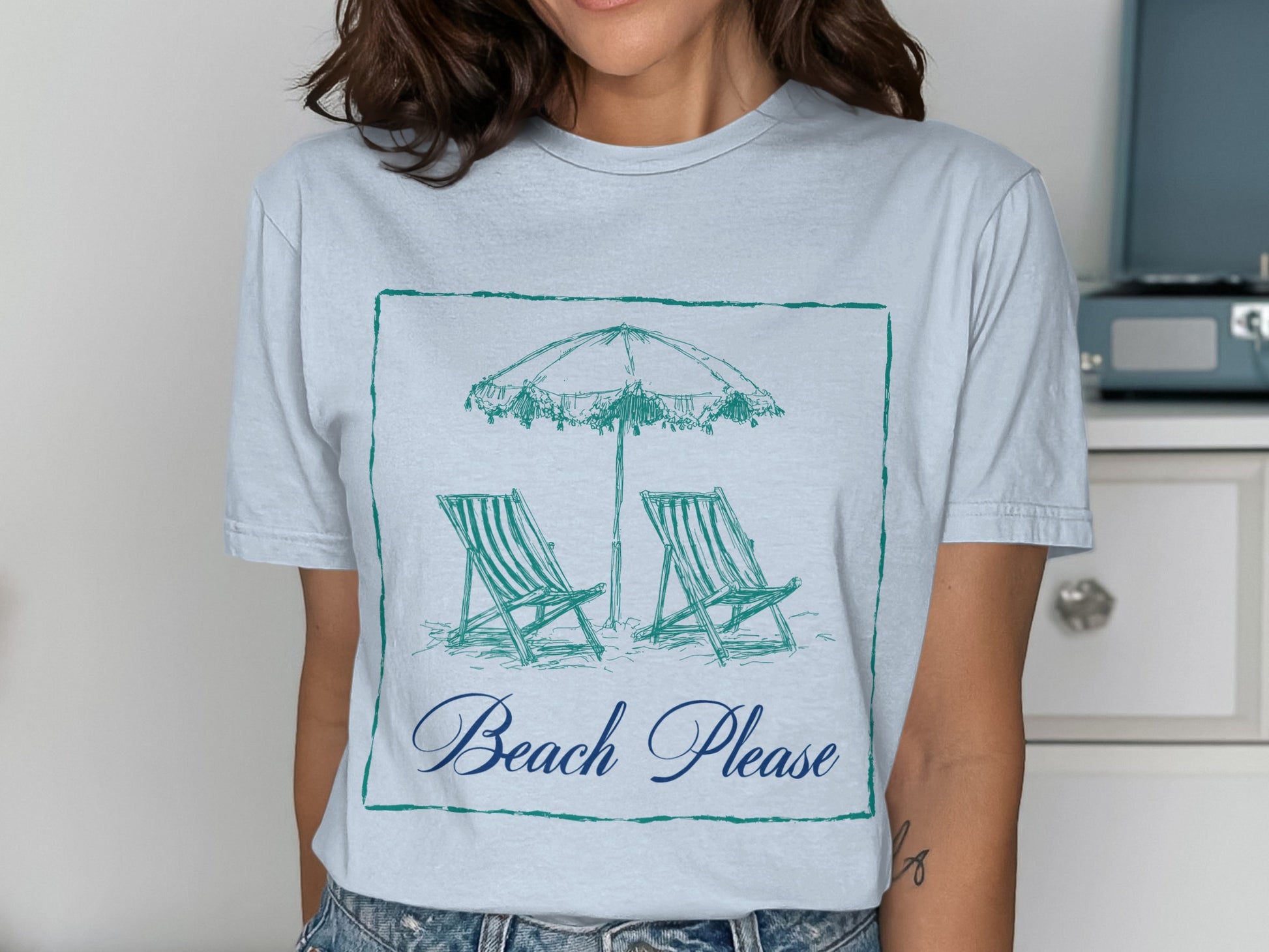 Light blue t-shirt with sketch of beach chairs and umbrella, "Beach Please" text.