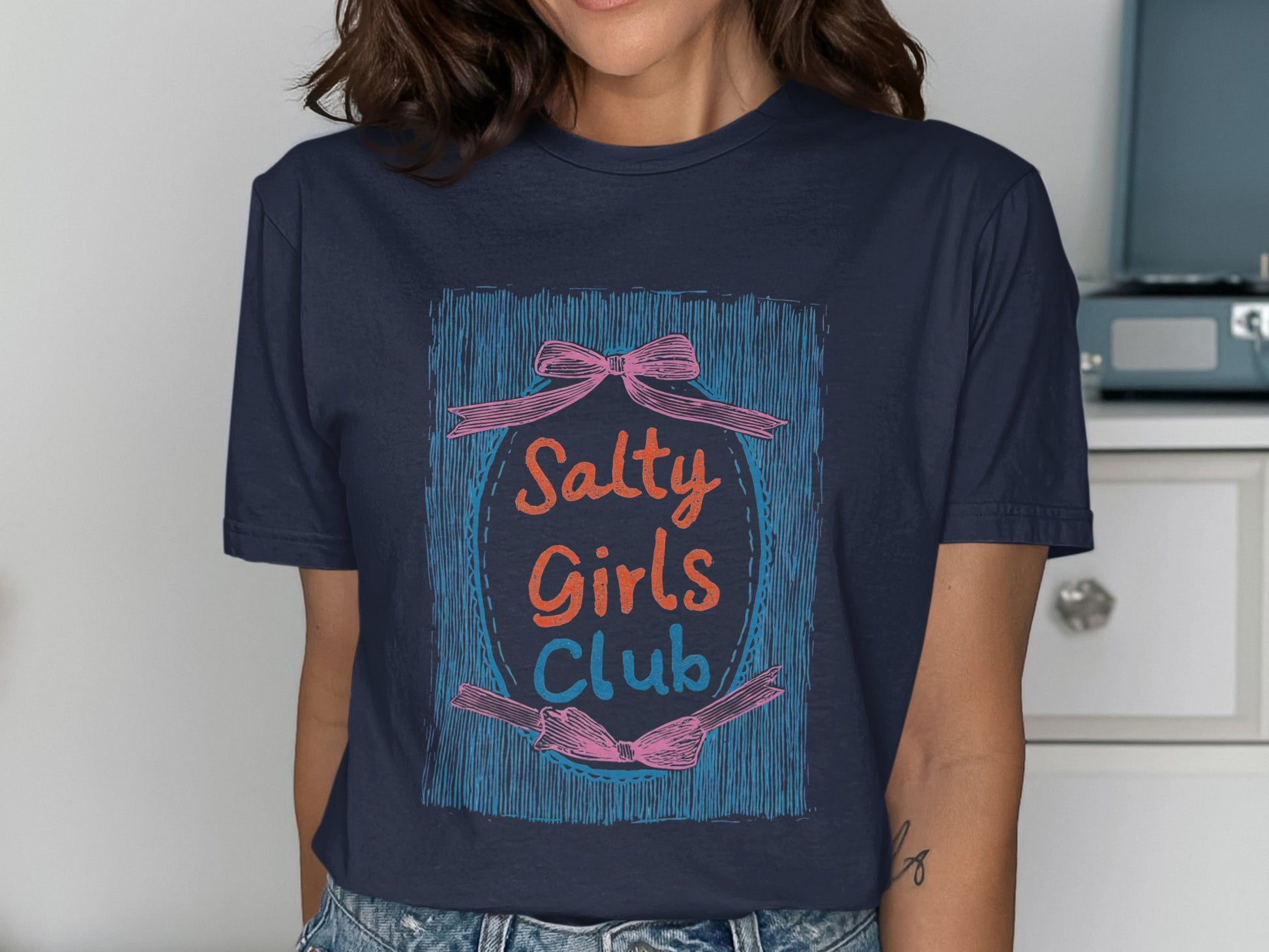 Navy t-shirt with "Salty Girls Club" text in a pink and orange oval with bows.