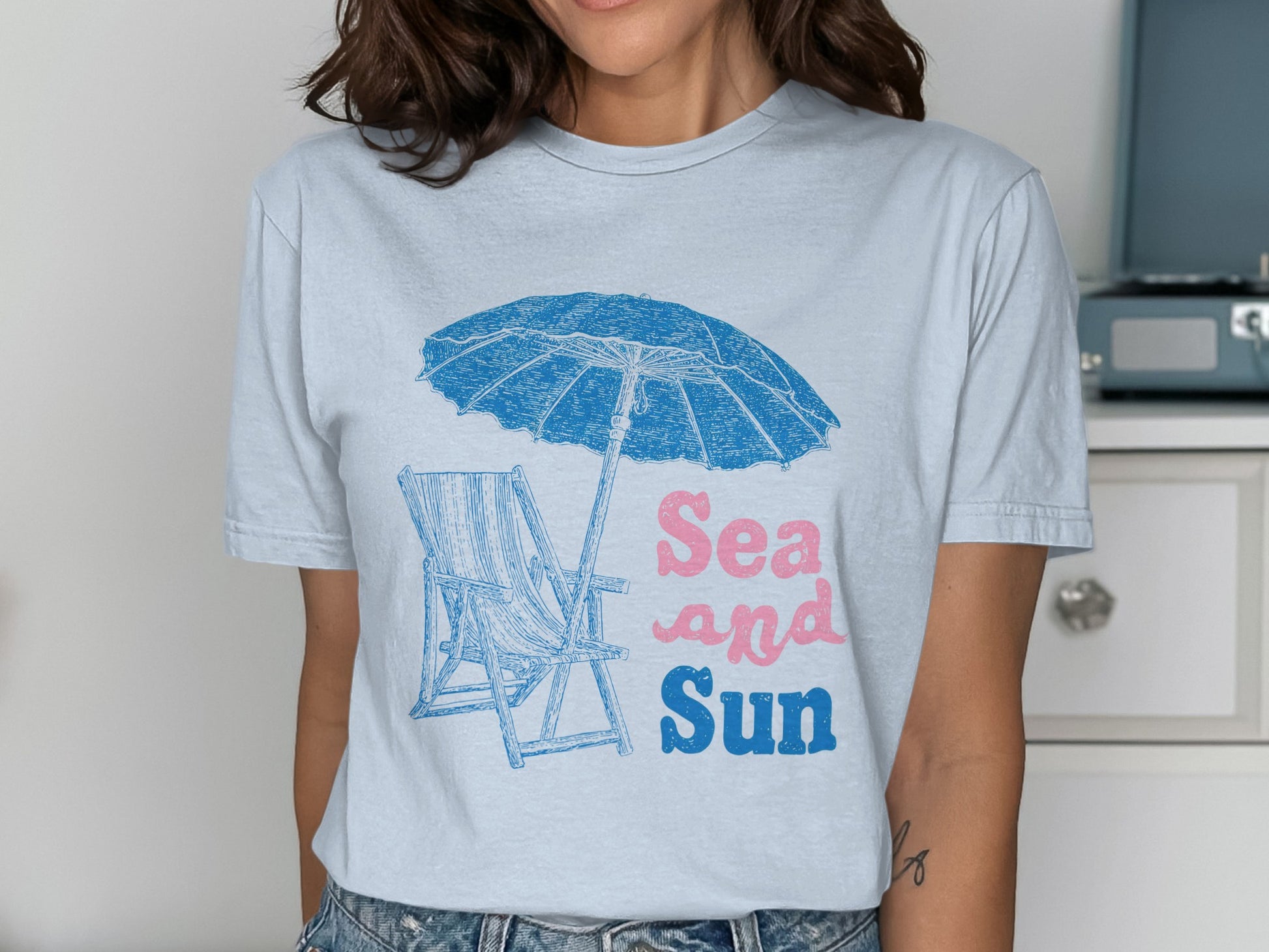 T-shirt with blue beach umbrella, chair, and "Sea and Sun" text.