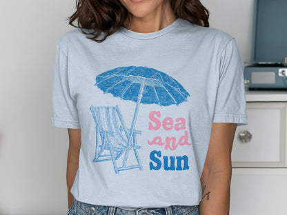 T-shirt with blue beach umbrella, chair, and "Sea and Sun" text.