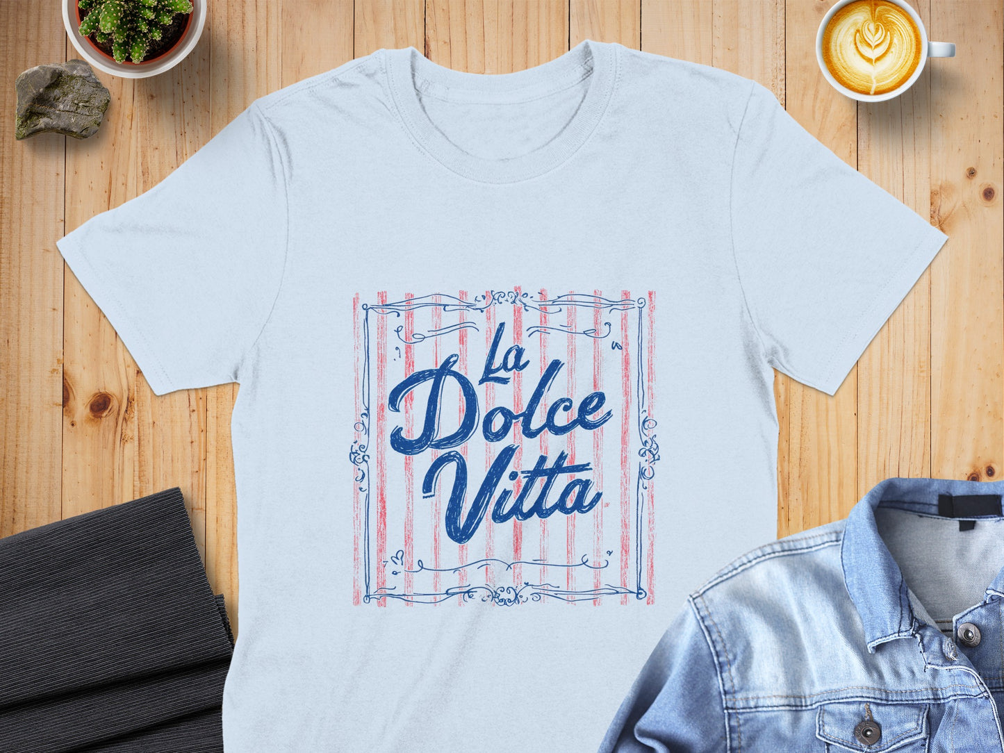 Light blue t-shirt with "La Dolce Vita" text in decorative blue font on a red striped background.