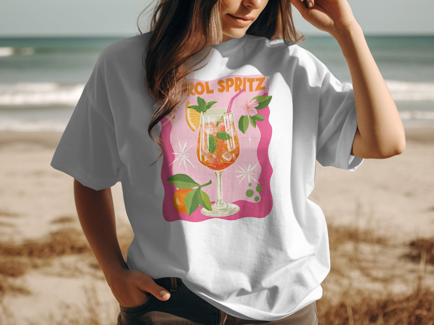 White t-shirt with "Aperol Spritz" cocktail illustration on beach background.