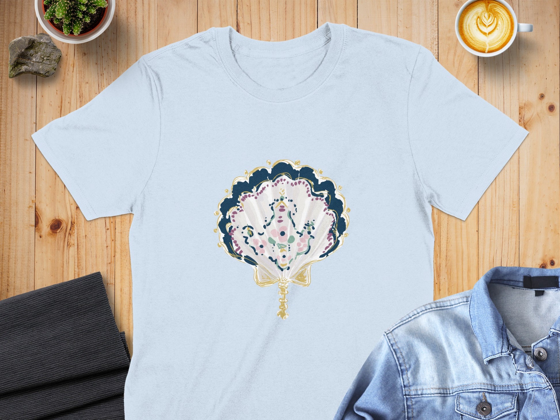 Light blue t-shirt with decorative shell illustration and gold ribbon.