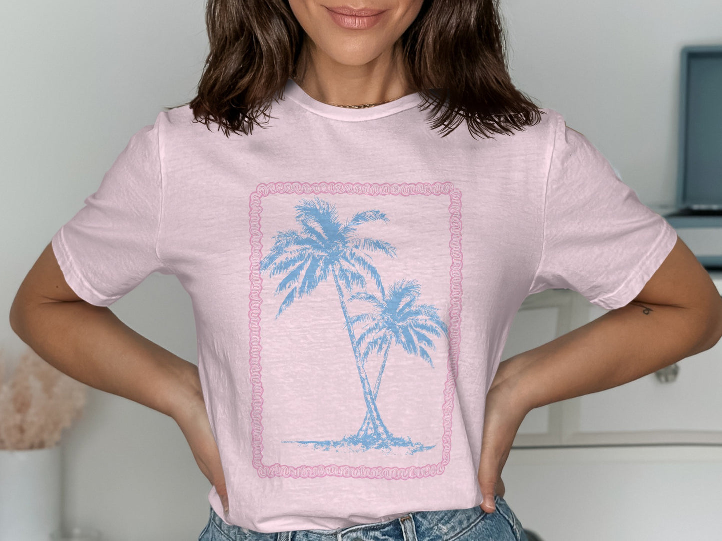 Light pink t-shirt with two blue palm trees inside a pink border.